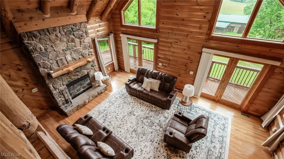 Living room with wood finished floors, french doors, high vaulted ceiling, a wood ceiling with exposed beams, and a stone fireplace