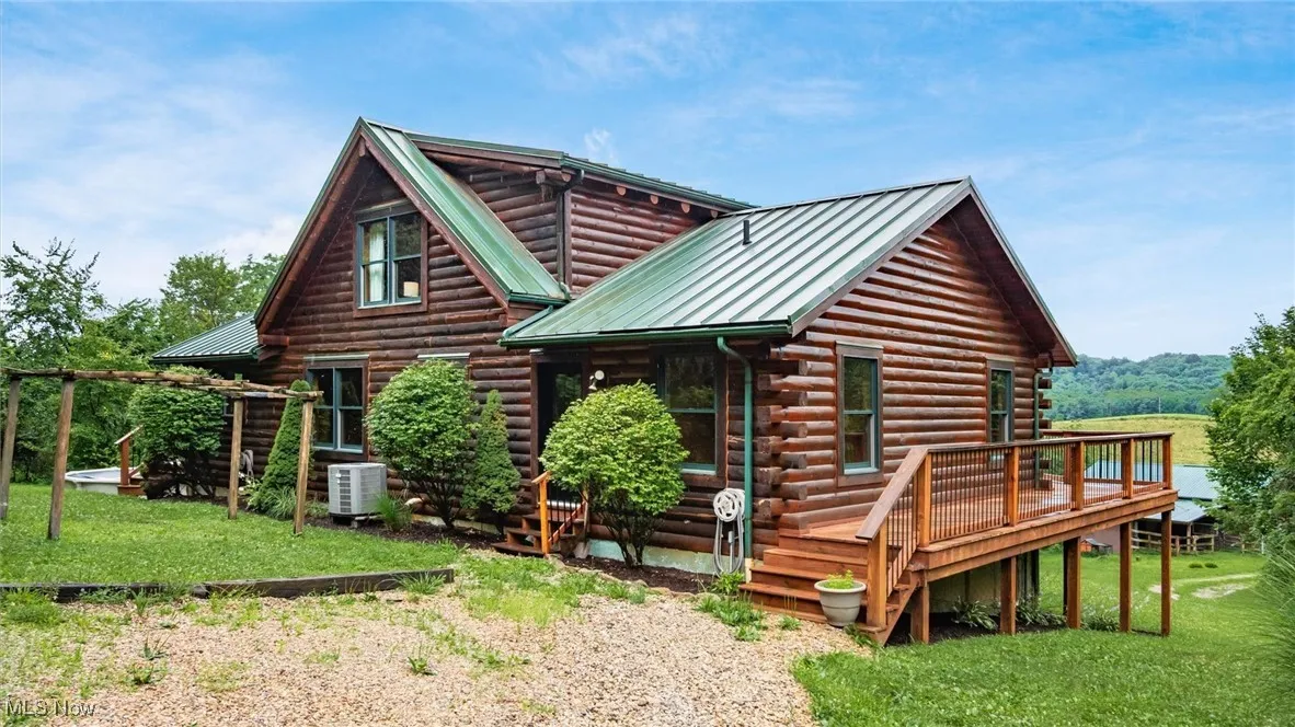 Back of house with log exterior, a metal roof, a wooden deck, and a yard