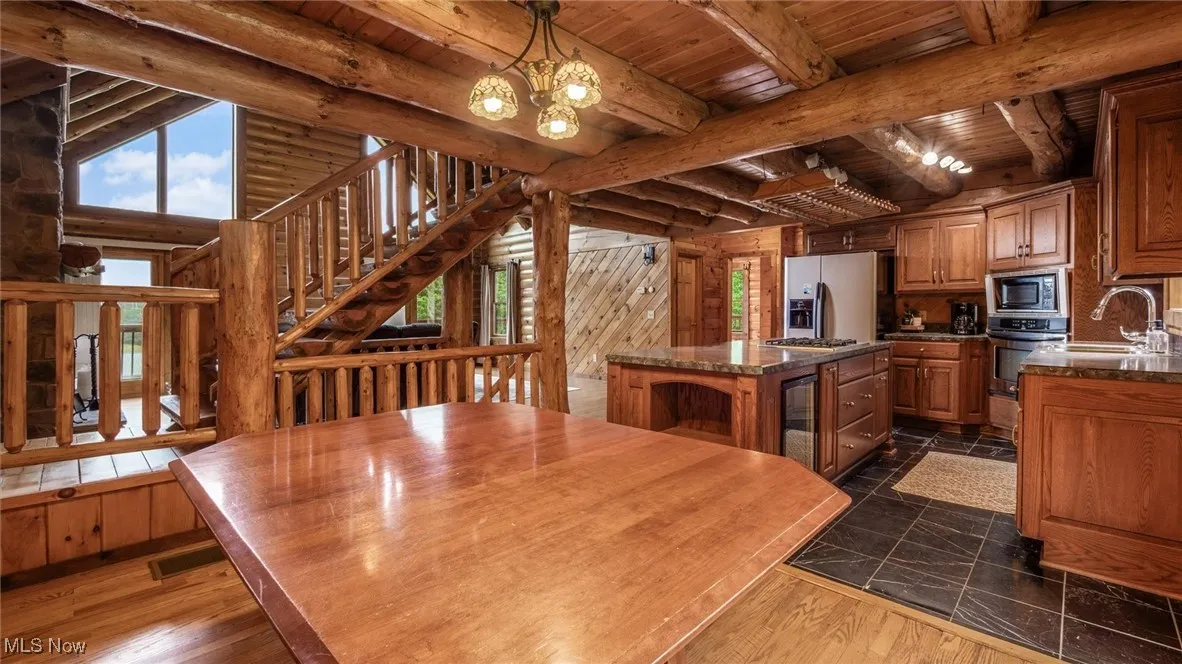 Kitchen with a chandelier, a center island, a wood ceiling with exposed beams, brown cabinets, and stainless steel appliances