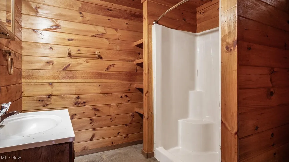 Bathroom with a shower, wooden walls, vanity, and unfinished concrete floors