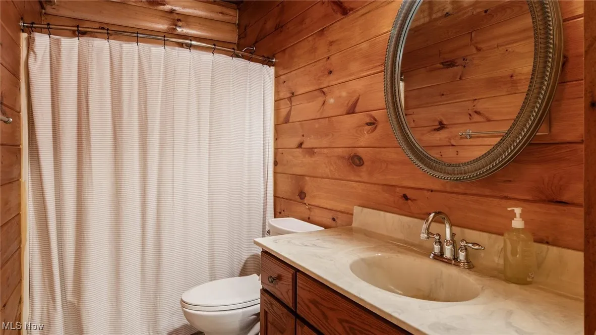 Full bath featuring wooden walls, vanity, and curtained shower