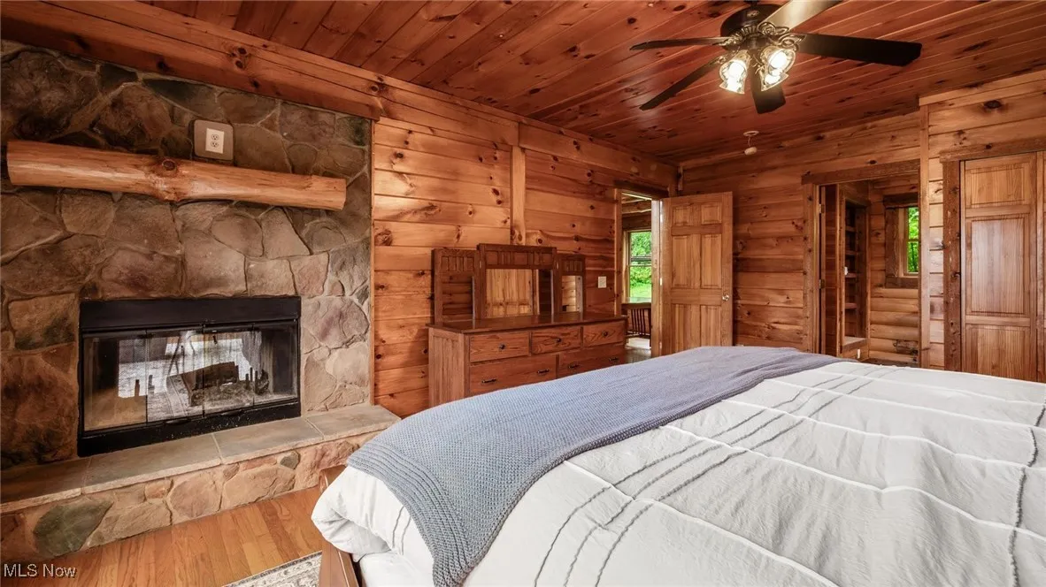Bedroom with wooden walls, wood finished floors, wooden ceiling, and a stone fireplace