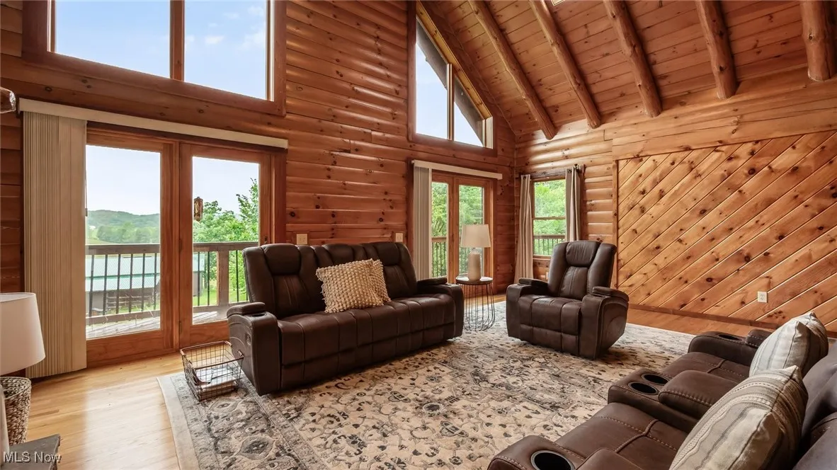 Living room with high vaulted ceiling, wood finished floors, a wooden ceiling with exposed beams, plenty of natural light, and log walls
