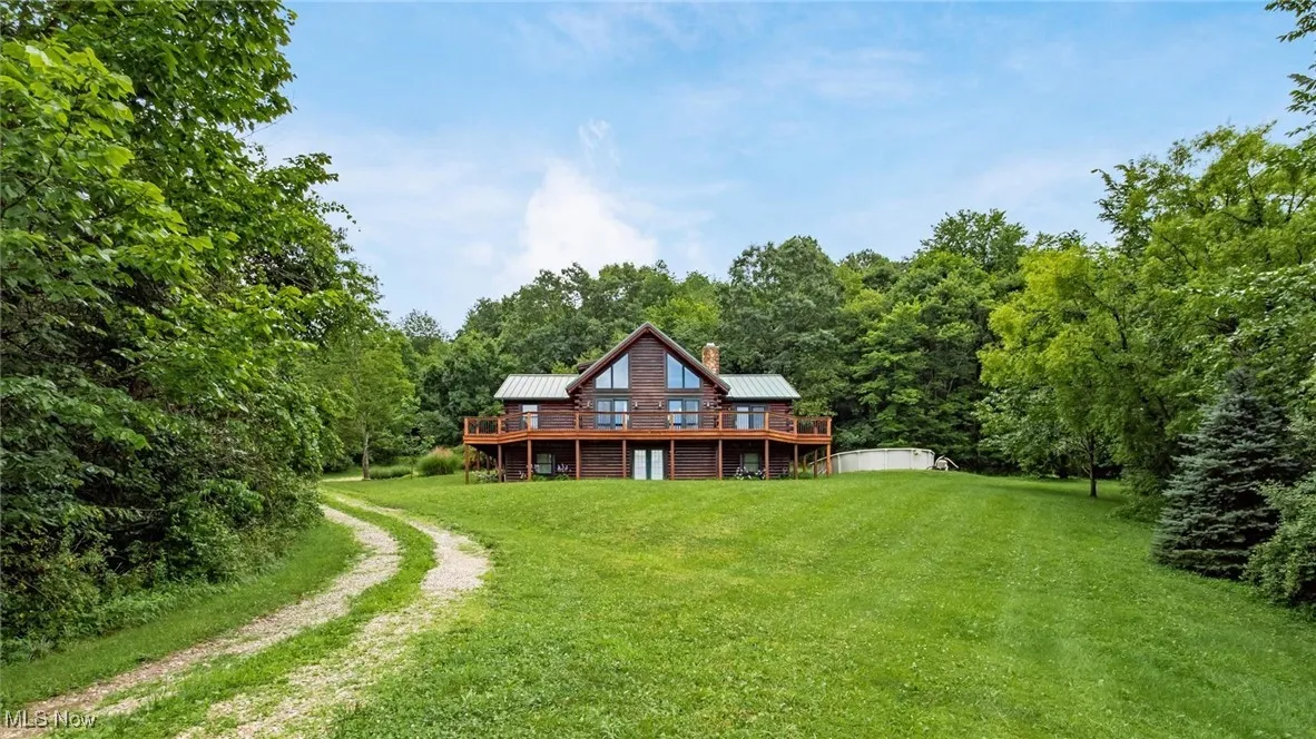 Rear view of house featuring a deck, a lawn, a metal roof, a chimney, and a view of trees