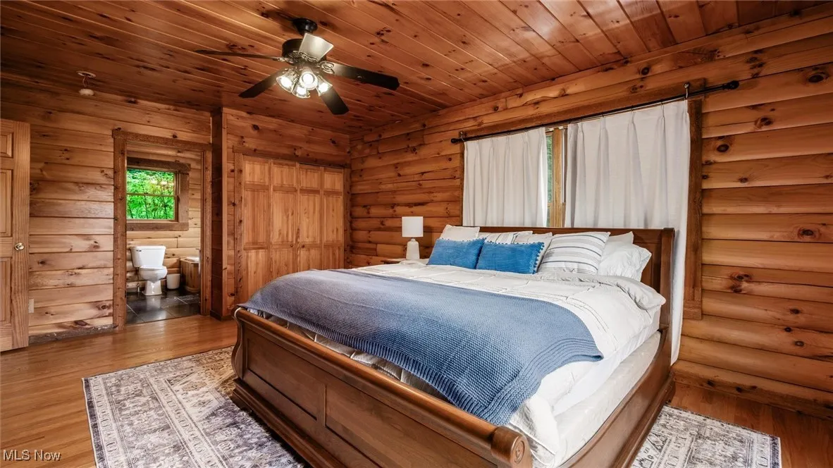 Bedroom featuring wood finished floors, ensuite bathroom, and rustic walls