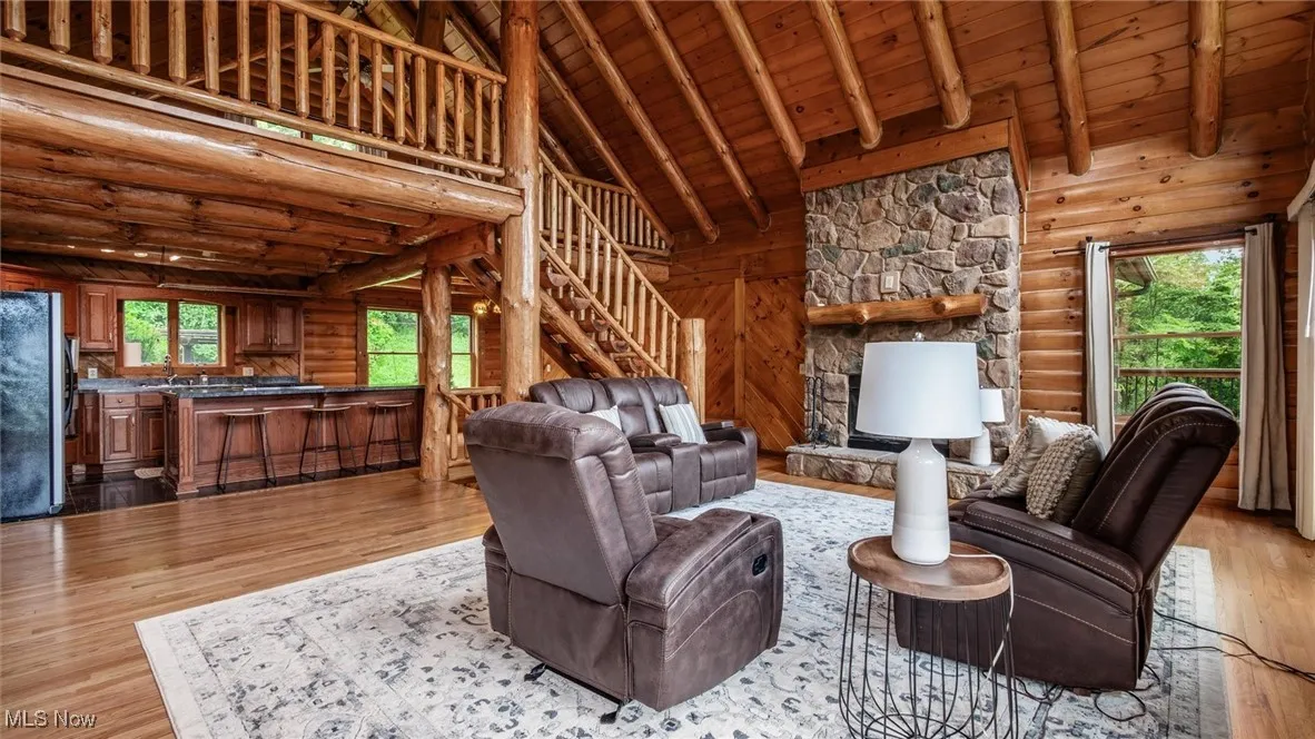 Living area with high vaulted ceiling, healthy amount of natural light, stairs, light wood-style flooring, and log walls