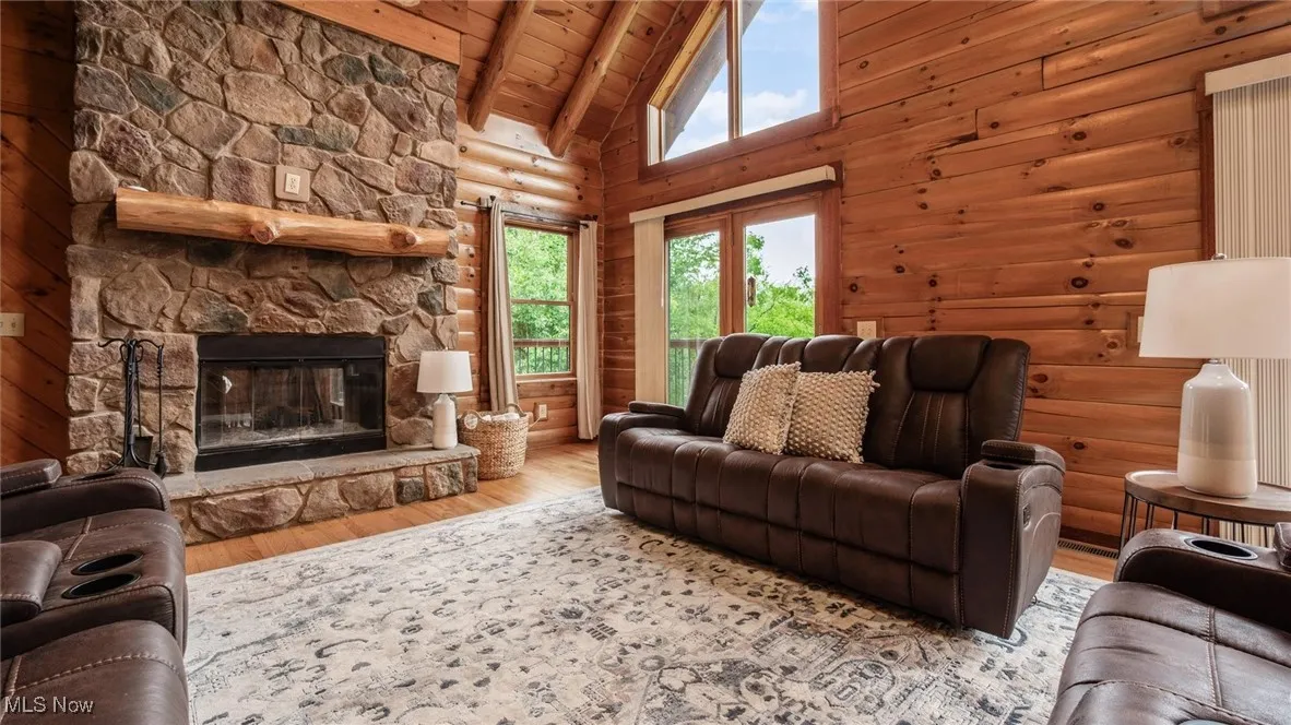 Living room with a wood ceiling with exposed beams, wood finished floors, a stone fireplace, and high vaulted ceiling