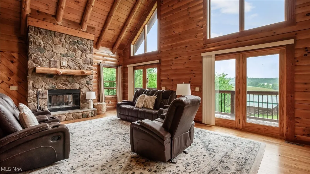 Living room featuring high vaulted ceiling, light wood-style flooring, a wooden ceiling with exposed beams, and a stone fireplace
