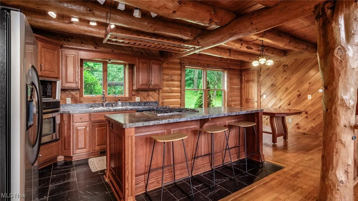 Kitchen with stainless steel appliances, plenty of natural light, a kitchen breakfast bar, a wooden ceiling with exposed beams, and hanging light fixtures