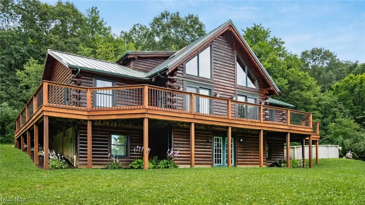 Rear view of house featuring a wooden deck, a yard, log exterior, and a metal roof