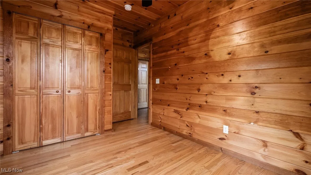Unfurnished bedroom featuring light wood finished floors, wood walls, and wood ceiling