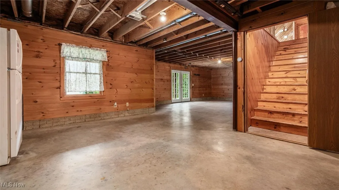 Basement with wooden walls, freestanding refrigerator, and stairway