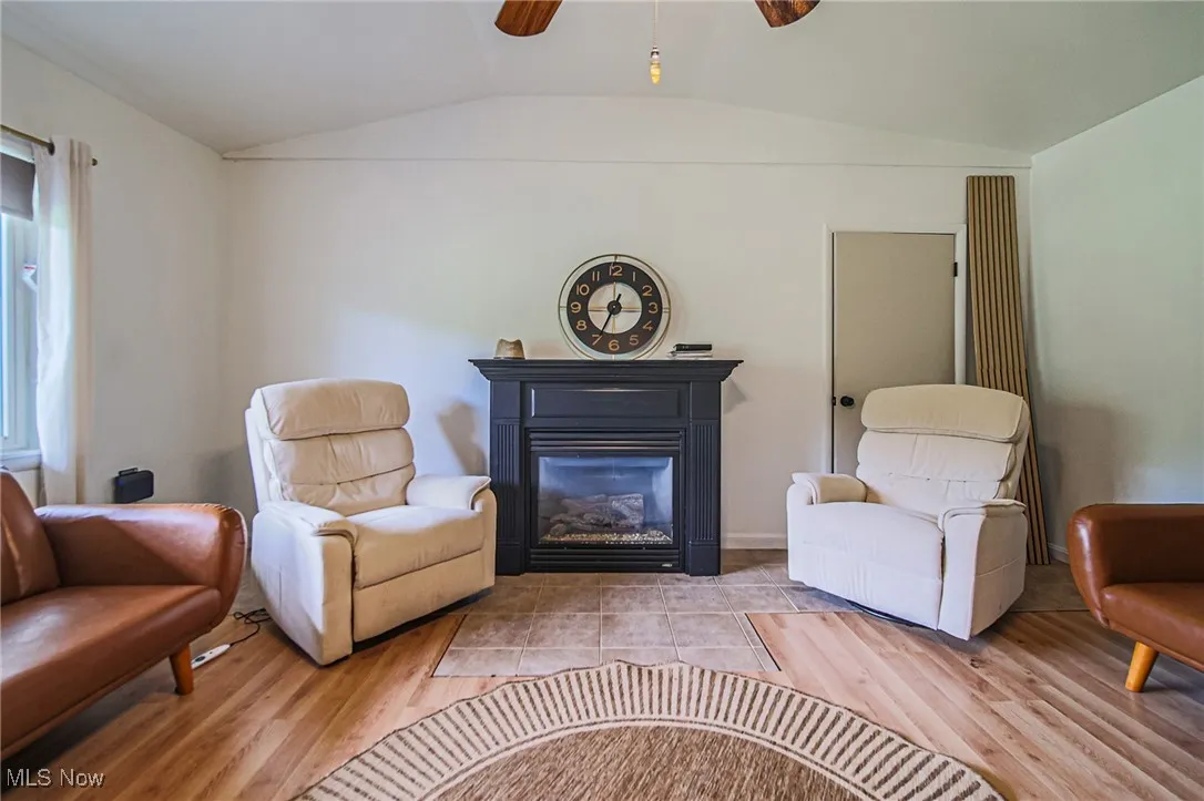 Living area featuring vaulted ceiling, a ceiling fan, wood finished floors, and a glass covered fireplace