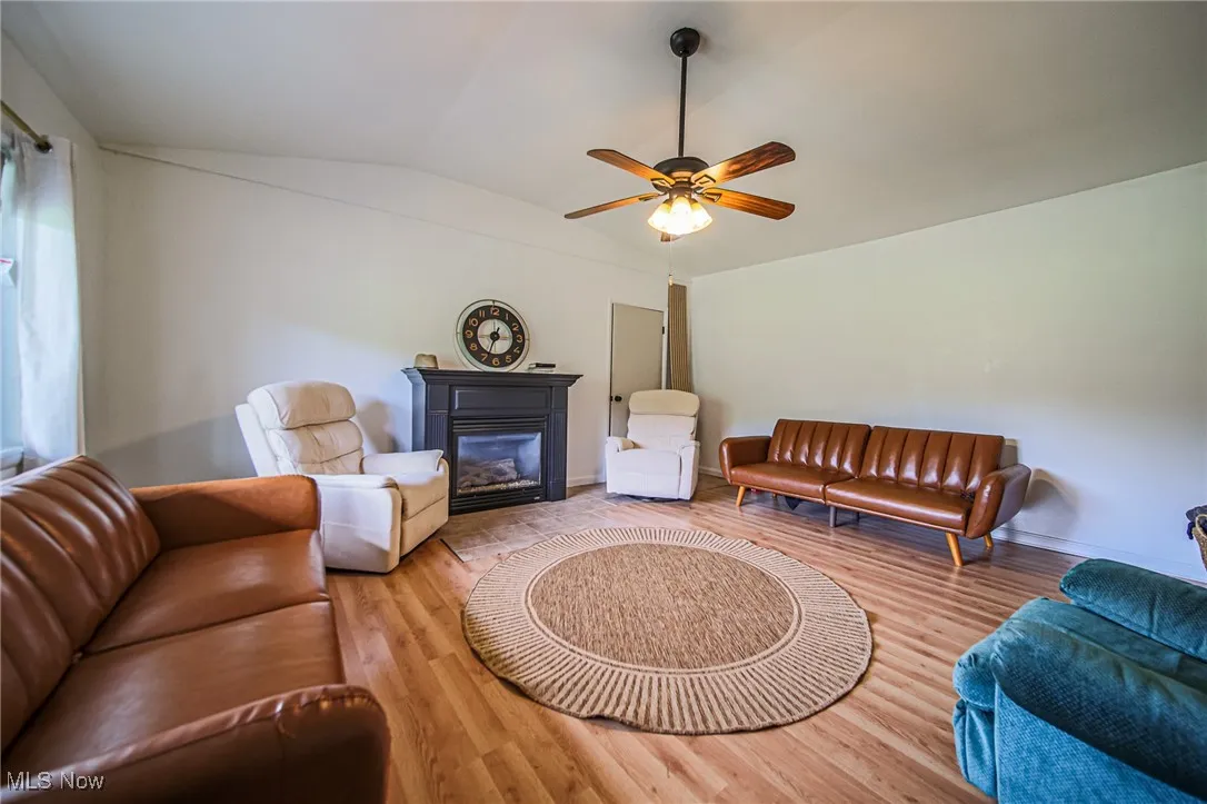 Living area with vaulted ceiling, a glass covered fireplace, ceiling fan, and wood finished floors