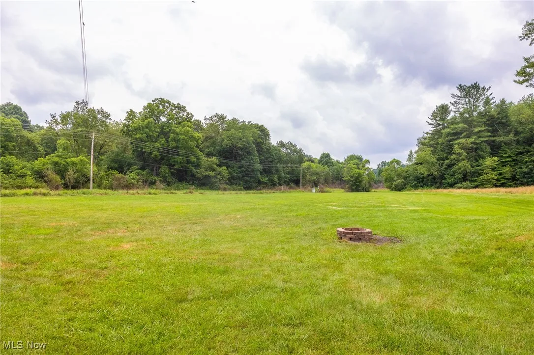 View of grassy yard featuring a fire pit and a view of trees
