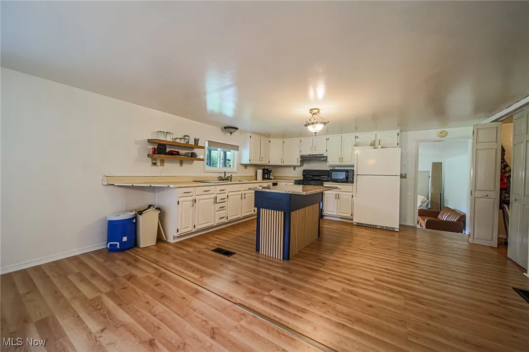 Kitchen featuring black appliances, a kitchen island, white cabinets, and light wood finished floors