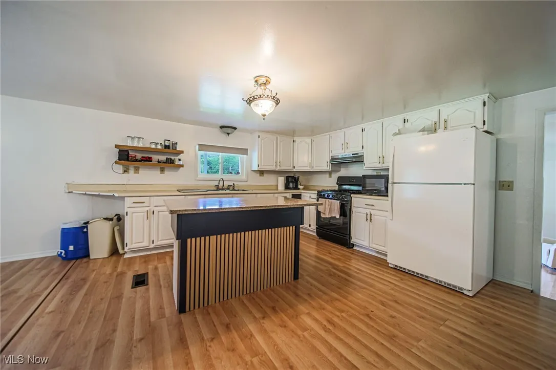 Kitchen featuring black appliances, open shelves, and white cabinetry