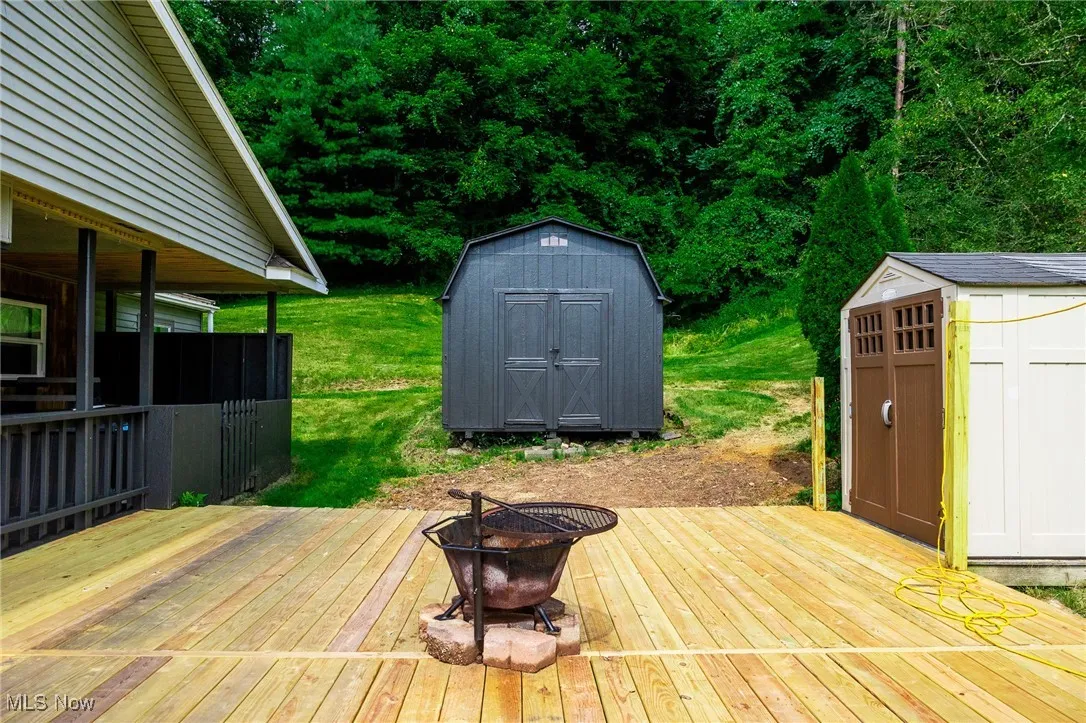 Wooden terrace featuring a storage shed, an outdoor fire pit, and a yard