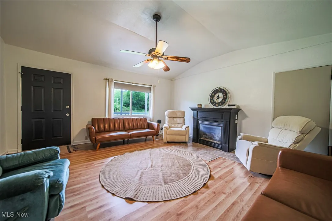 Living area featuring vaulted ceiling, a ceiling fan, wood finished floors, and a glass covered fireplace