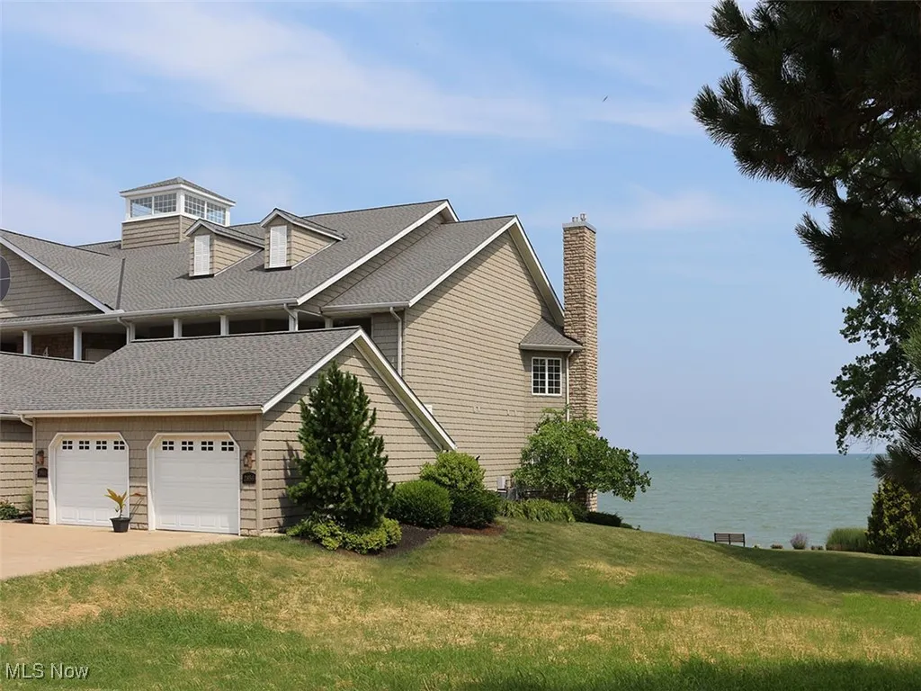 View of property exterior with a lawn, driveway, a water view, a chimney, and an attached garage