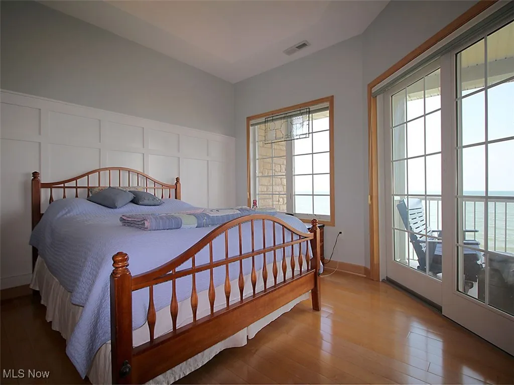 Owner's suite featuring multiple wood flooring, with sliders leading to balcony with unobstructed lake views