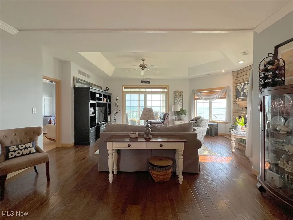 Living room featuring a raised ceiling, wood finished floors, ceiling fan, and a floor to ceiling stone hearth gas fireplace