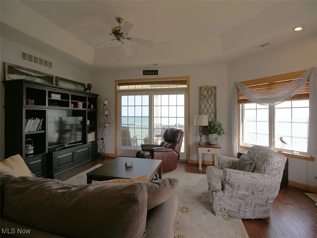 Living area with a ceiling fan, wood finished floors, a tray ceiling, and recessed lighting with bay windows with views of lake
