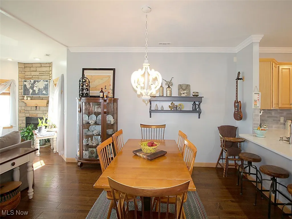 Dining area with dark wood-style flooring, a chandelier, ornamental molding, and a fireplace