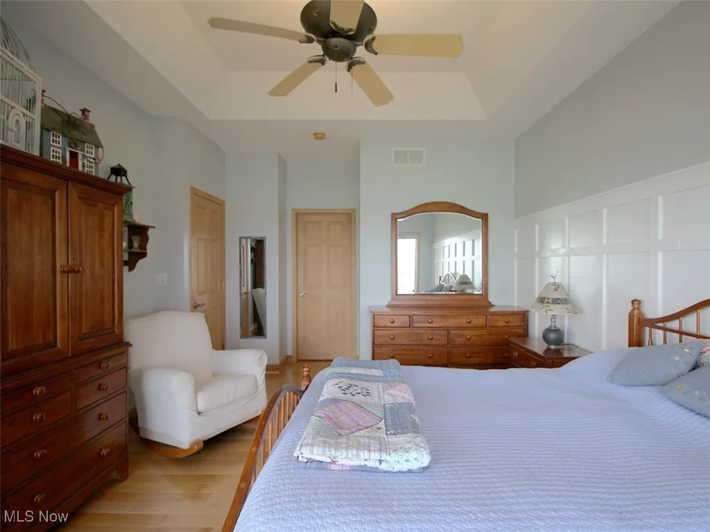 Owner's suite  featuring a raised ceiling, light wood flooring, and ceiling fan