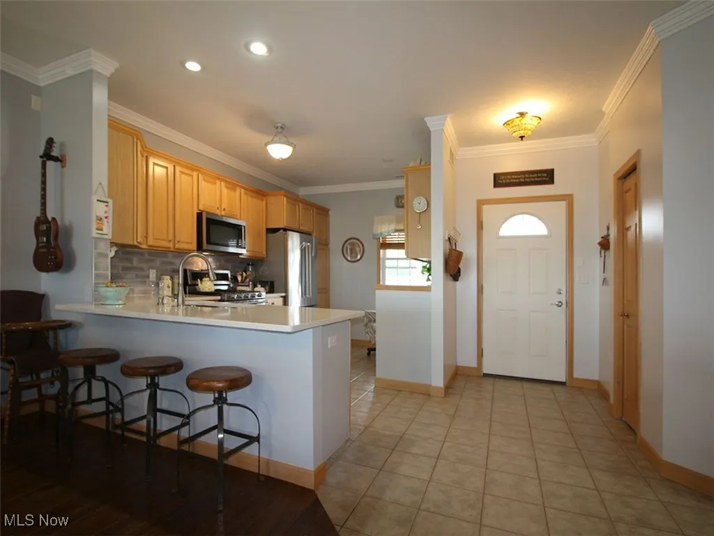 Kitchen featuring a peninsula, appliances with stainless steel finishes, tasteful backsplash, crown molding, and granite countertops