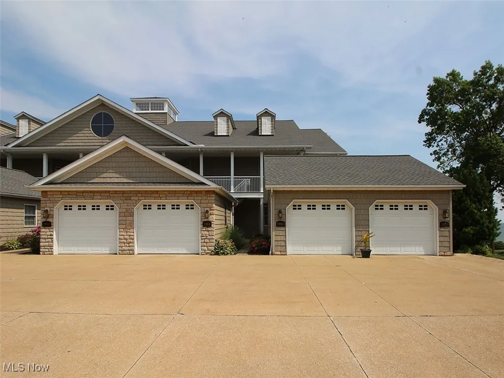 View of front of property featuring concrete driveway, stone siding, a garage, a shingled roof, and a balcony