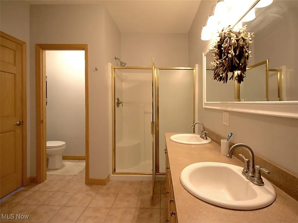 Owner's bathroom  featuring a stall shower, commode closet, ceramic tile, and double vanity
