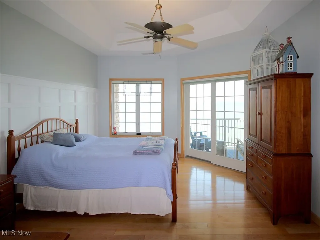 Owner's suite with a raised ceiling, light wood flooring, access to balcony,ceiling fan and tray ceiling