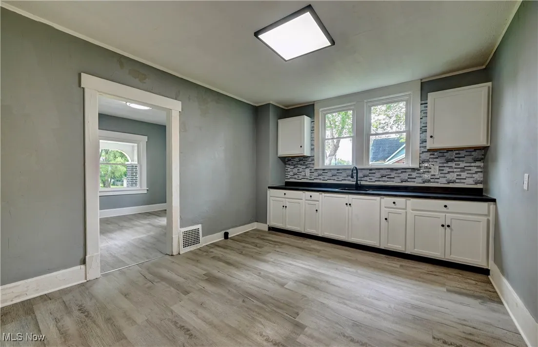 Kitchen featuring decorative backsplash, dark countertops, plenty of natural light, light wood-style floors, and crown molding