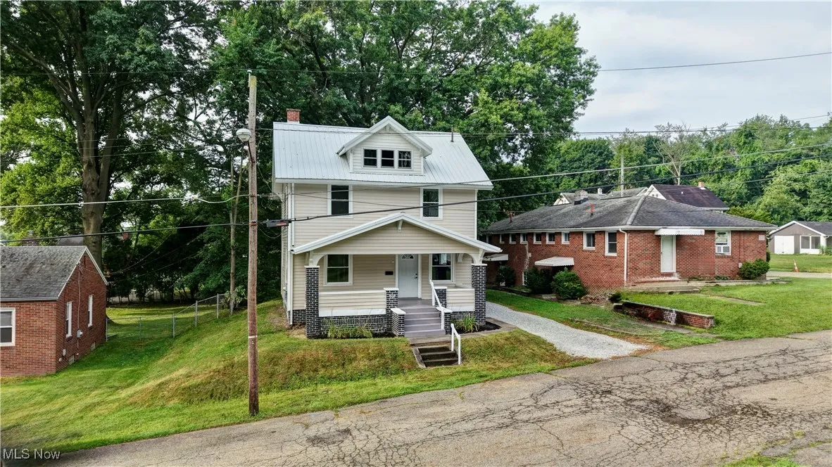 American foursquare style home featuring covered porch, a front lawn, a chimney, driveway, and a metal roof