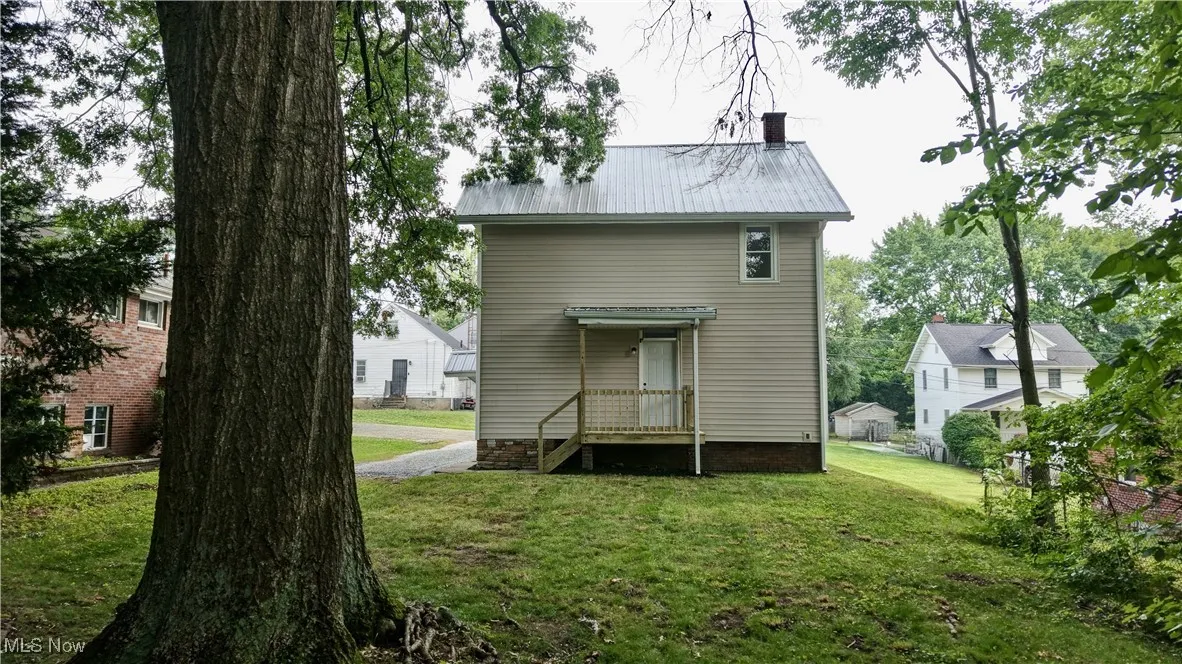 Rear view of house with a chimney, a lawn, and a metal roof