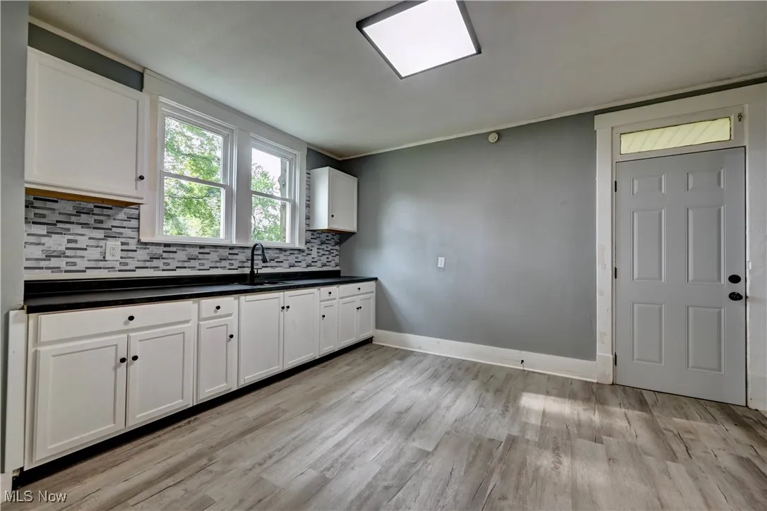 Kitchen featuring dark countertops, backsplash, light wood-style flooring, and white cabinetry