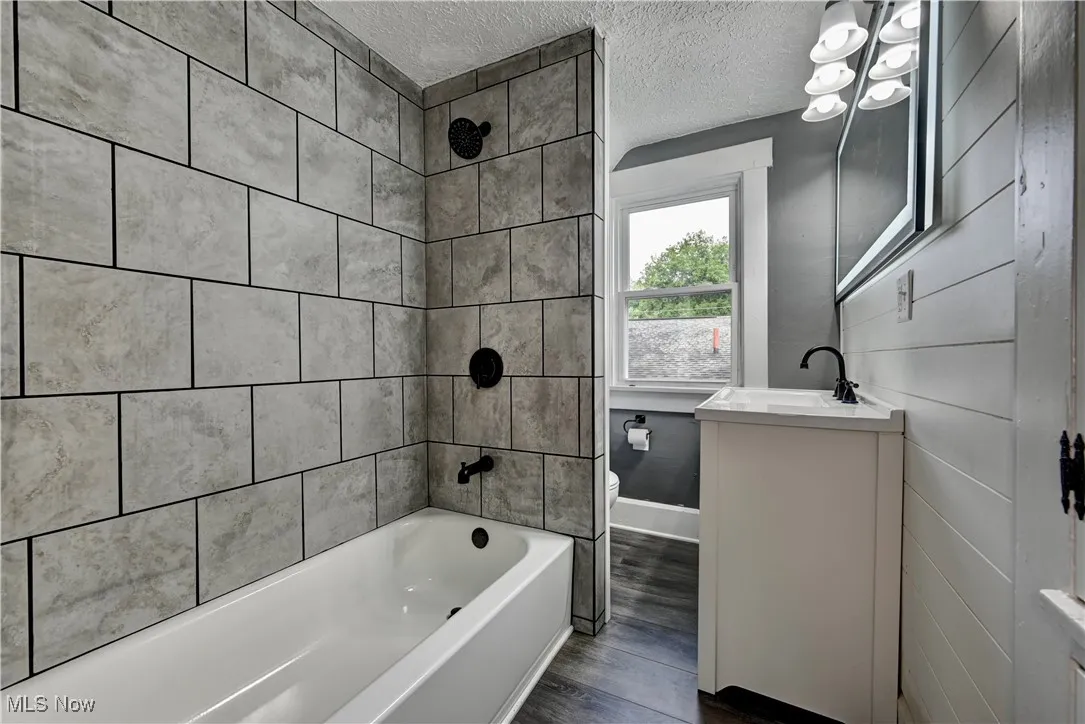 Full bath featuring wood finished floors, vanity, shower / bath combination, and a textured ceiling