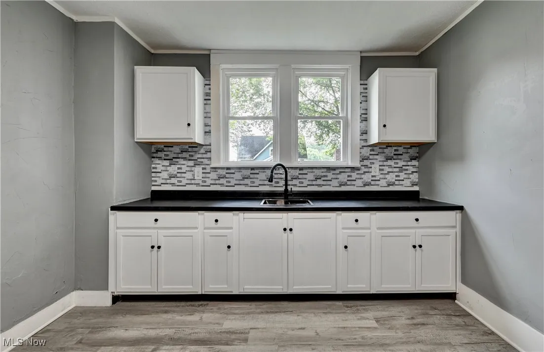 Kitchen with decorative backsplash, dark countertops, white cabinets, ornamental molding, and light wood-type flooring