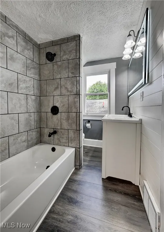 Full bath with vanity, shower / bath combination, wood finished floors, and a textured ceiling
