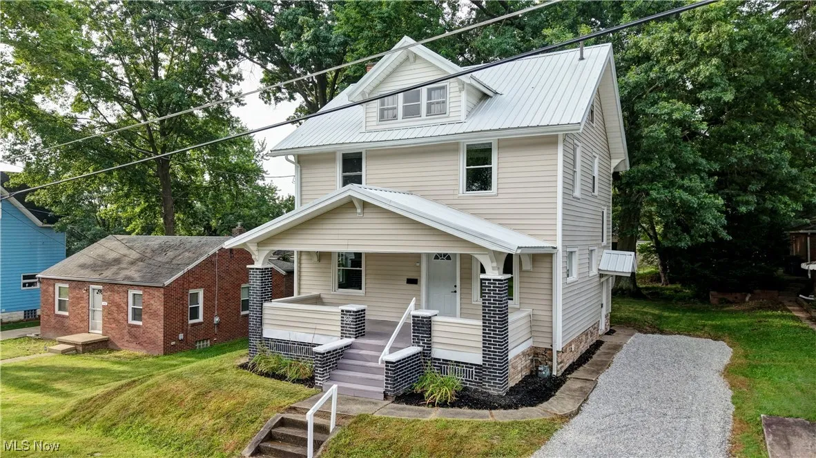 American foursquare style home featuring covered porch, a front lawn, and a metal roof