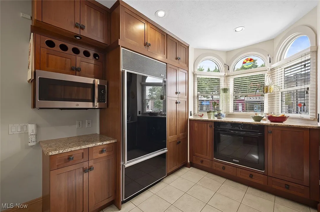 Kitchen featuring oven, refrigerator, brown cabinets, stainless steel microwave, and light stone counters