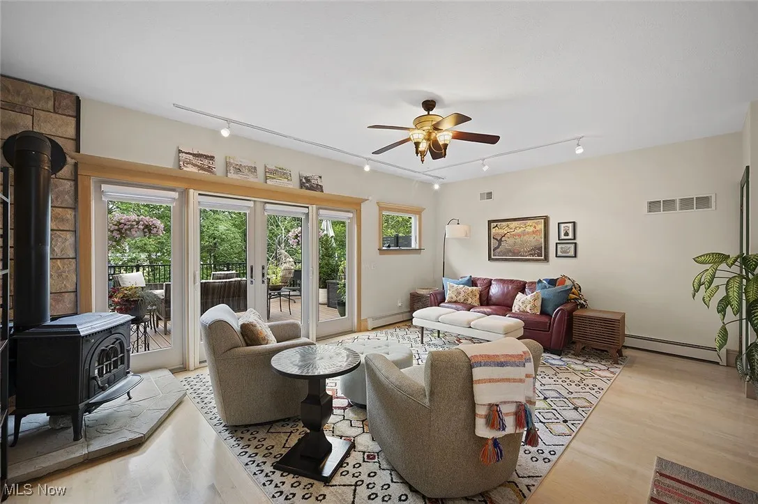 Living room featuring rail lighting, ceiling fan, light wood finished floors, and a wood stove