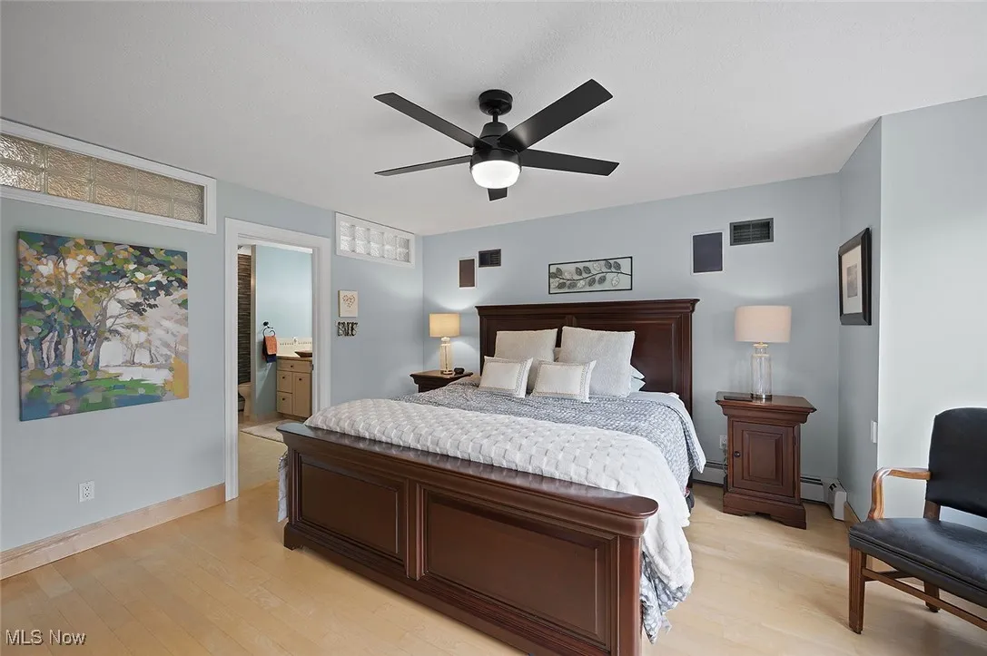 Bedroom featuring light wood finished floors, a ceiling fan, connected bathroom, and a baseboard radiator