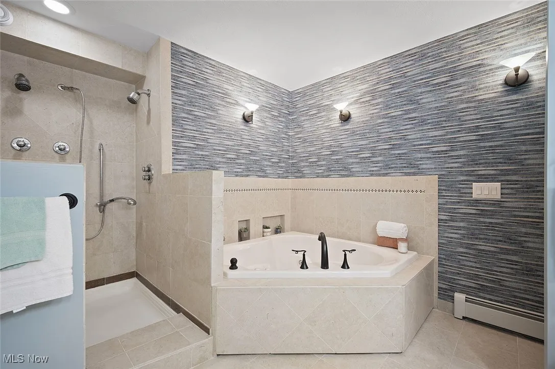 Bathroom featuring tile walls, a baseboard heating unit, tile patterned flooring, a bath, and walk in shower