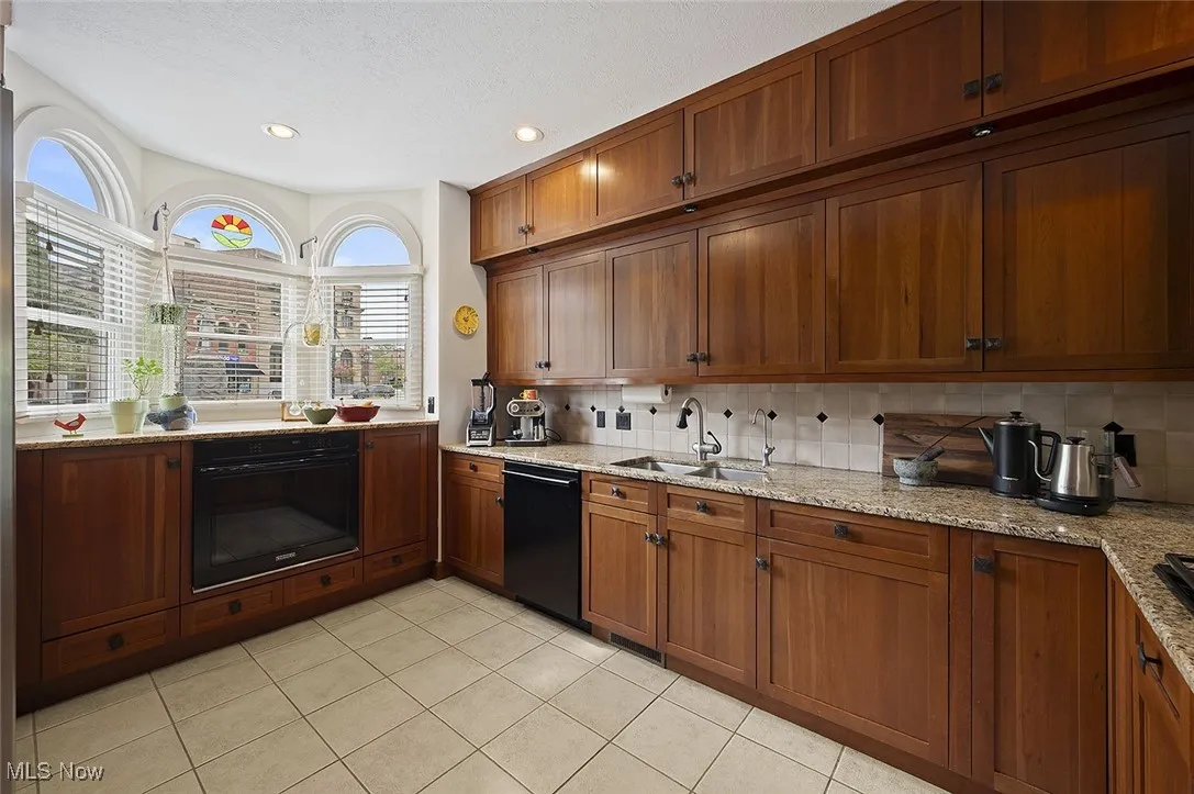 Kitchen featuring black appliances, tasteful backsplash, brown cabinets, light tile patterned floors, and recessed lighting