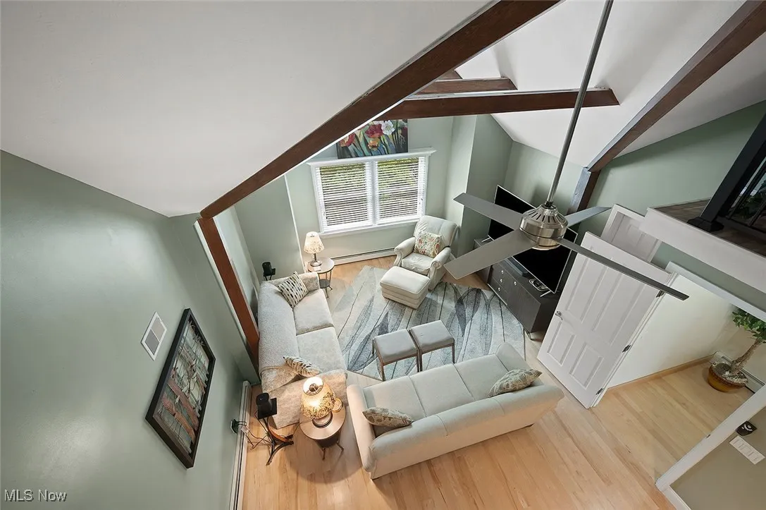 Living room featuring vaulted ceiling, wood finished floors, a ceiling fan, and baseboard heating