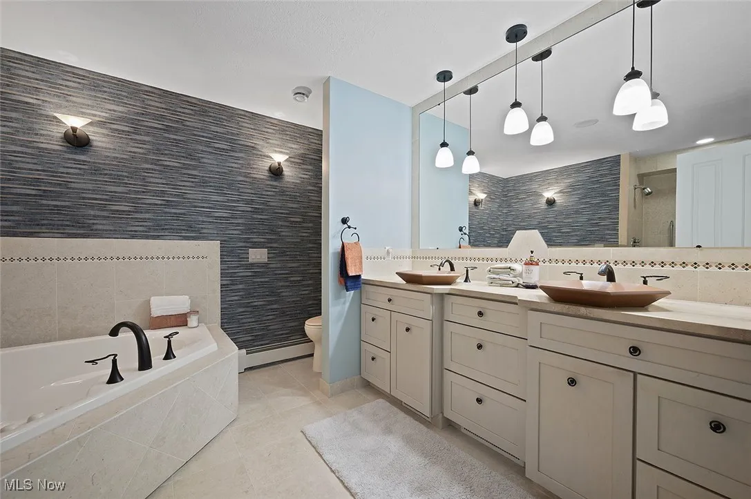 Full bath featuring double vanity, tile patterned floors, a bath, tiled shower, and baseboard heating
