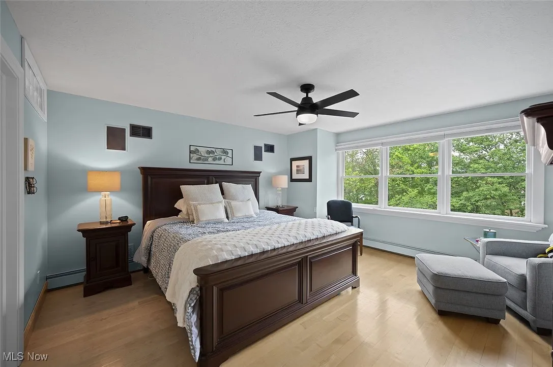 Bedroom with light wood finished floors, baseboard heating, and a ceiling fan