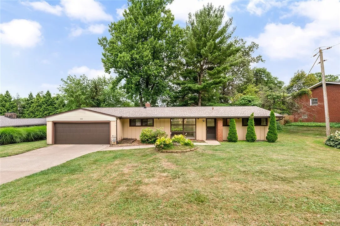 Single story home with a garage, concrete driveway, a front lawn, board and batten siding, and a chimney
